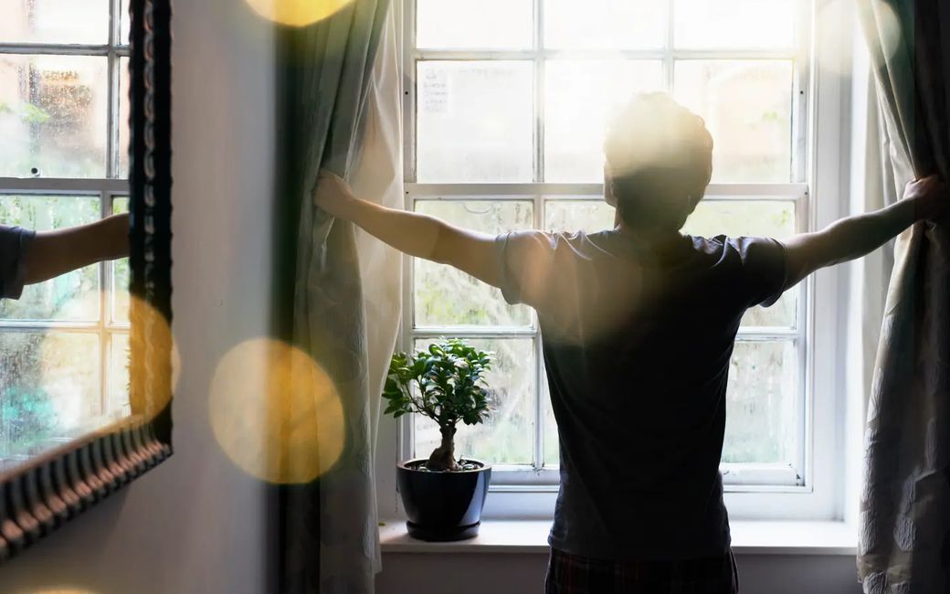Bewoner opent de gordijnen in een lichte, comfortabele kamer
